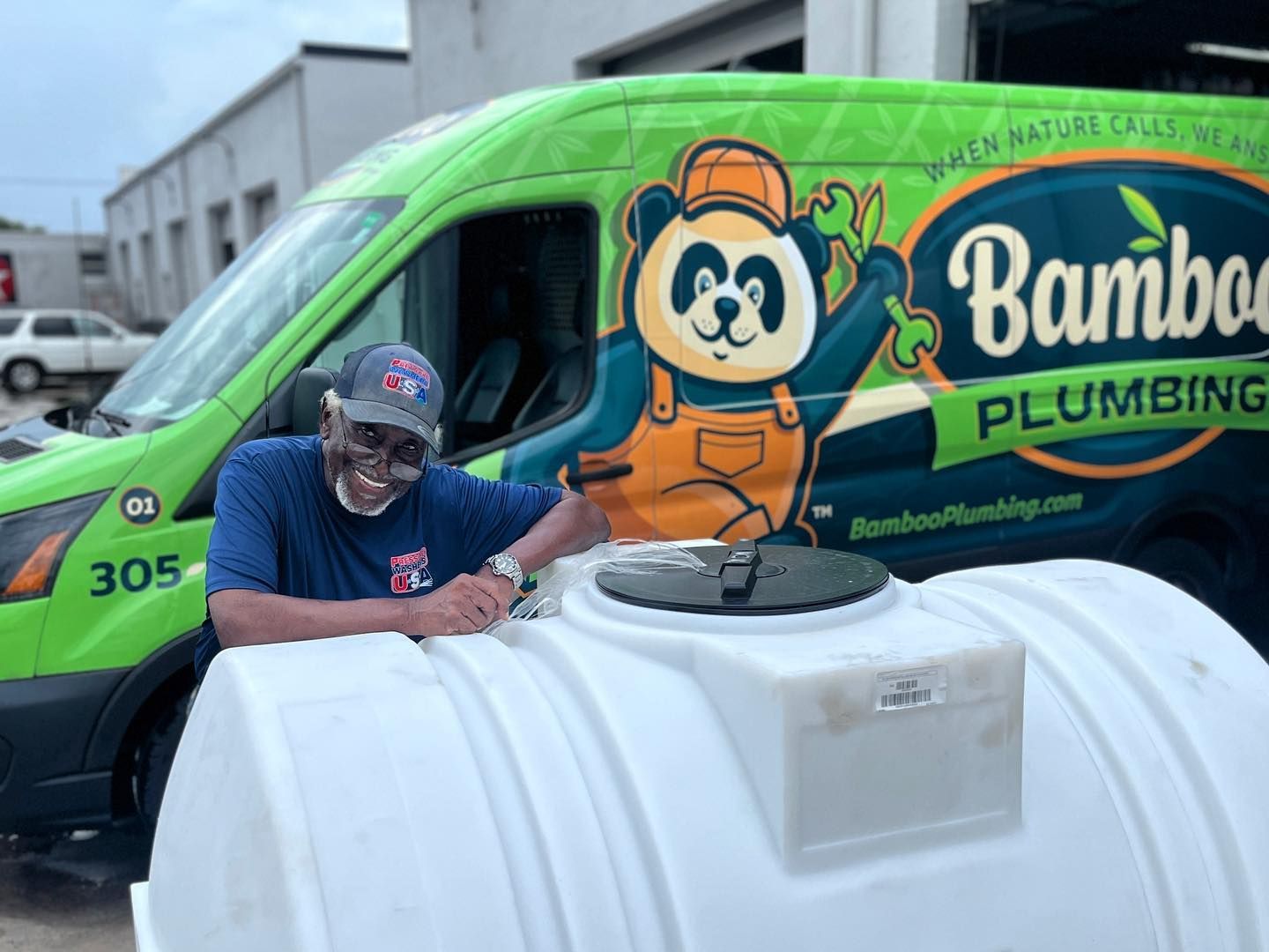 Man posing by a green Bamboo Plumbing van and a large white tank outdoors