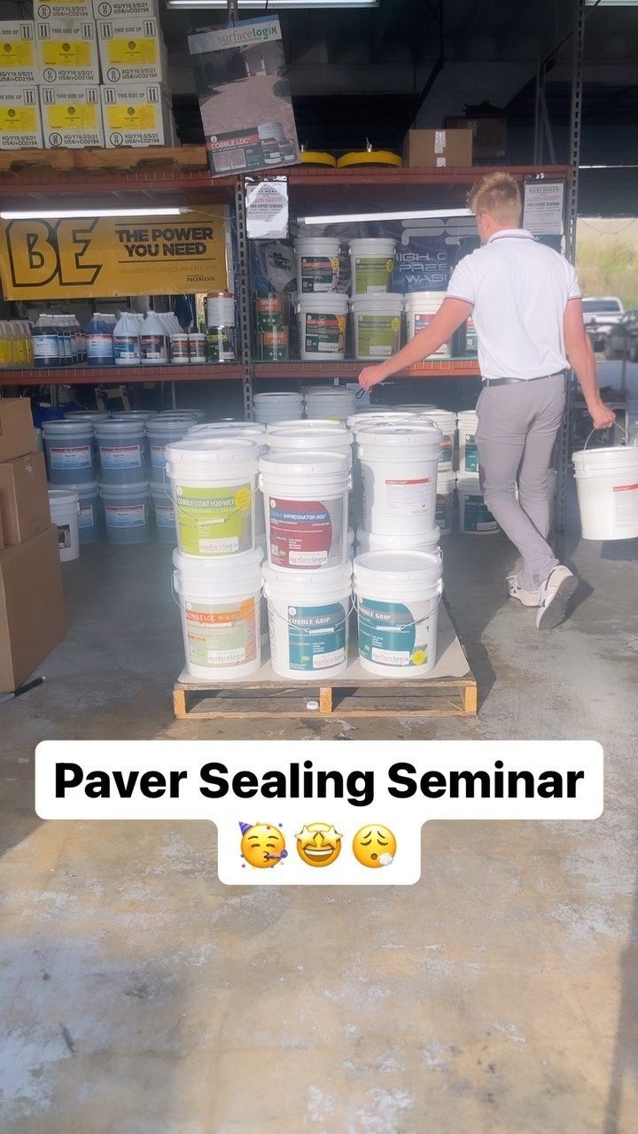 Man in white shirt loading white paver sealant buckets in a hardware store aisle, labeled “Paver Sealing Seminar”