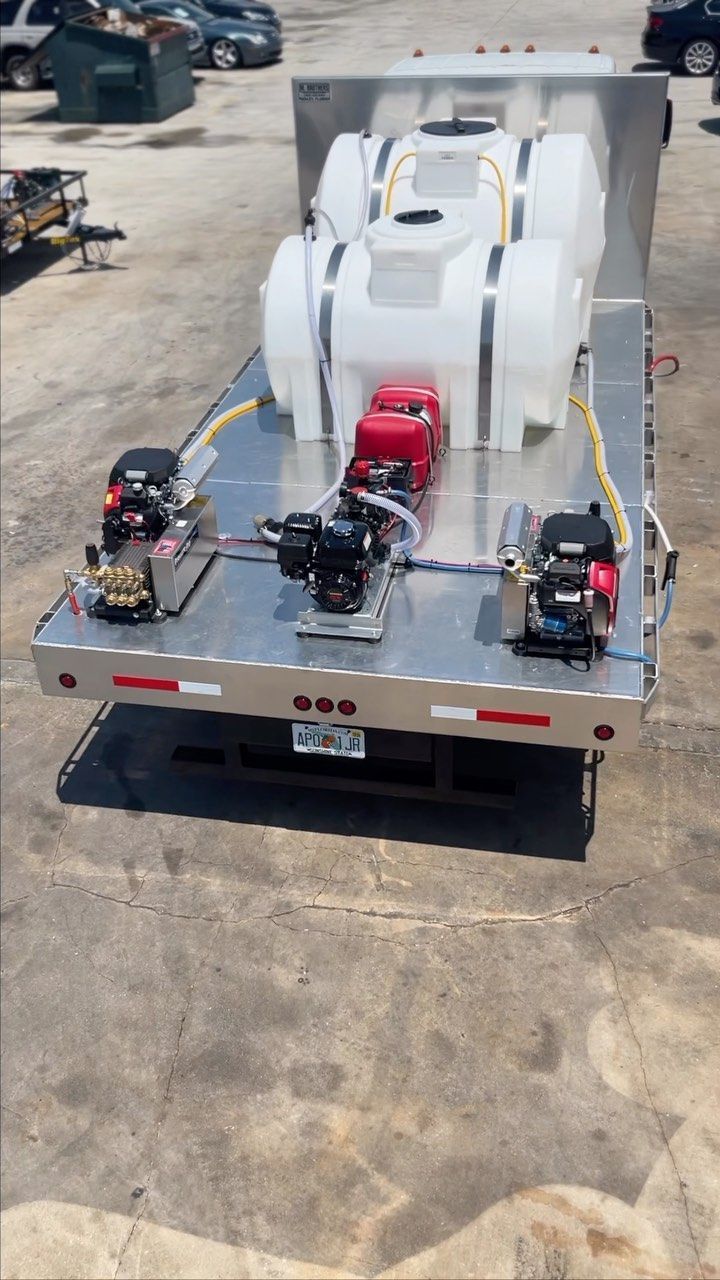 Flatbed trailer carrying large white industrial equipment and two red-and-black machines strapped on the back.