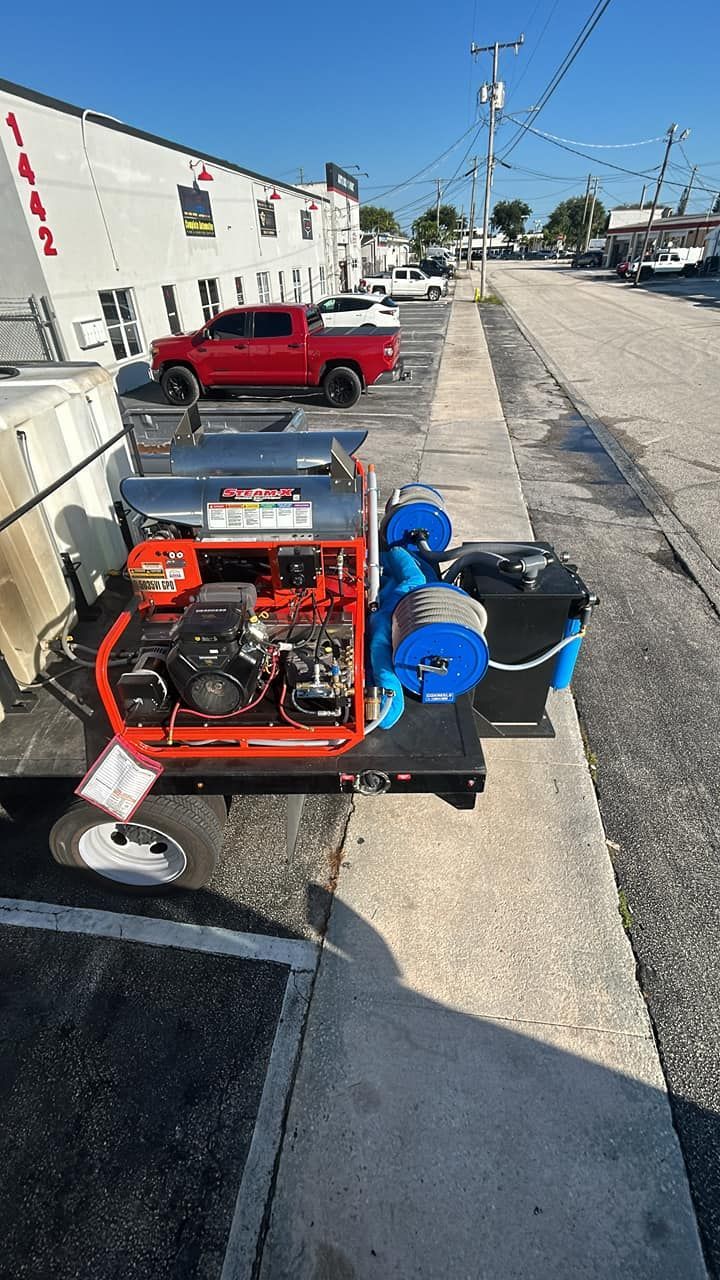 Red portable generator with blue water pumps on a curb beside a street and parked red pickup truck.