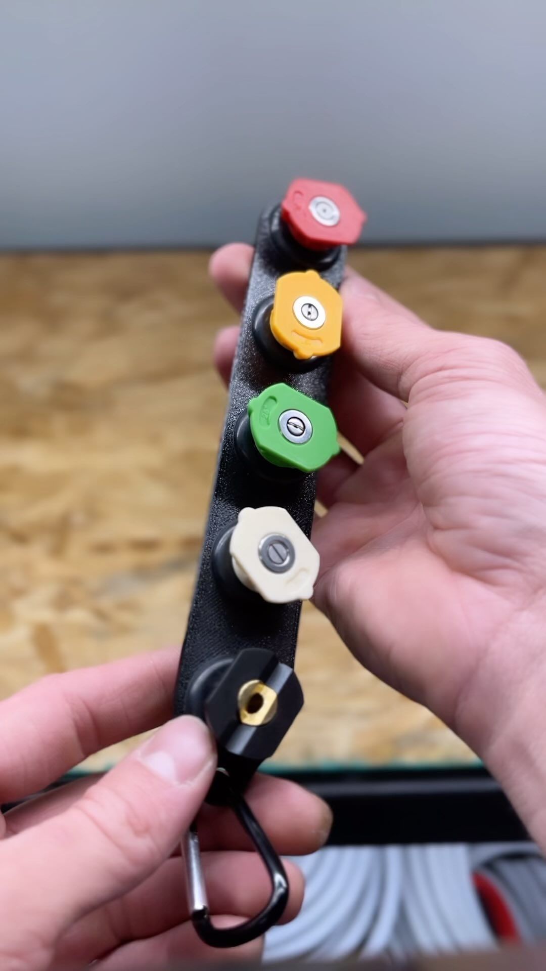 Hand holding a black leather key organizer with four colorful key heads: red, yellow, green, and white.