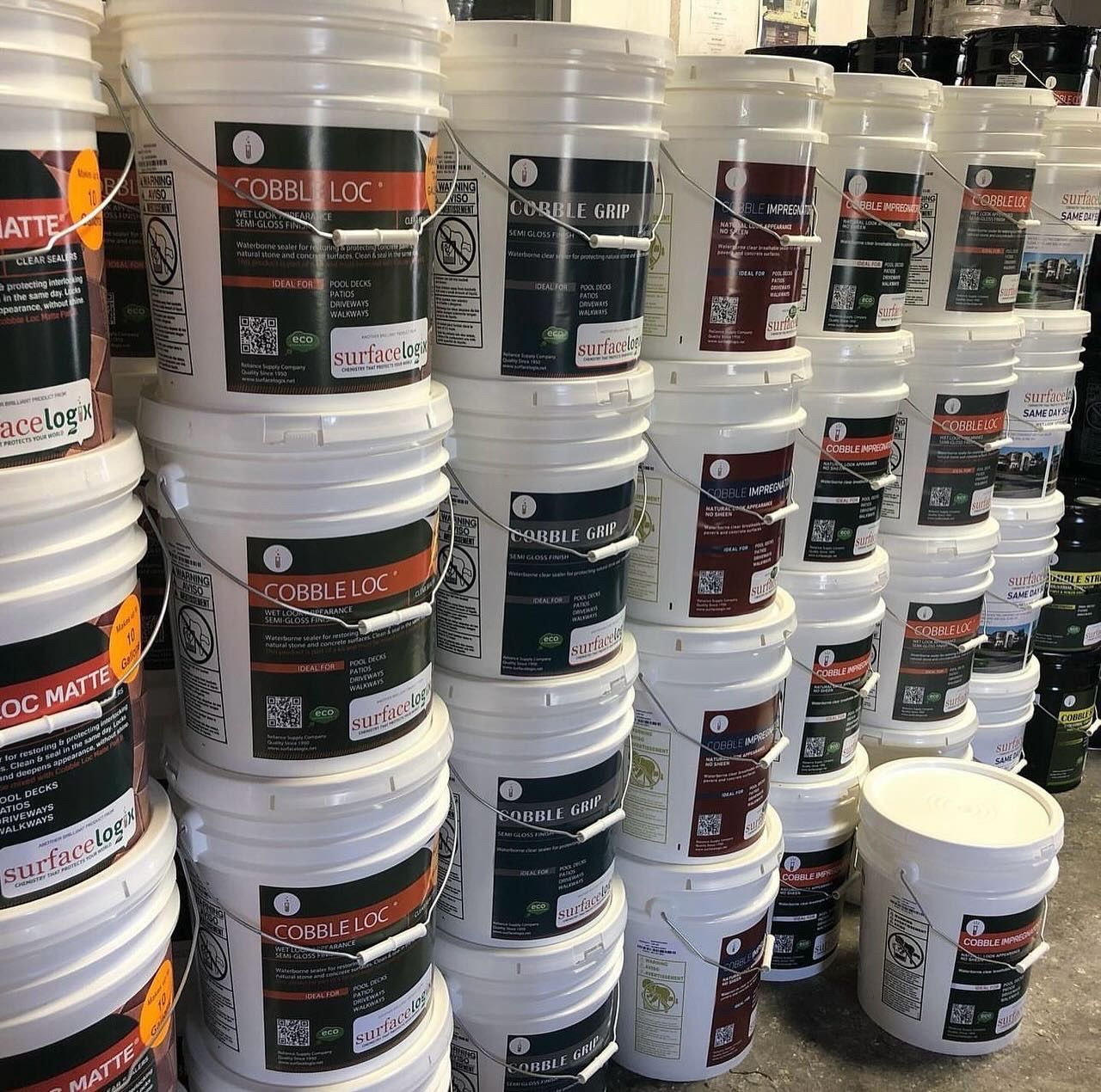 Stacks of white plastic buckets with black and red labels, arranged on warehouse shelves.