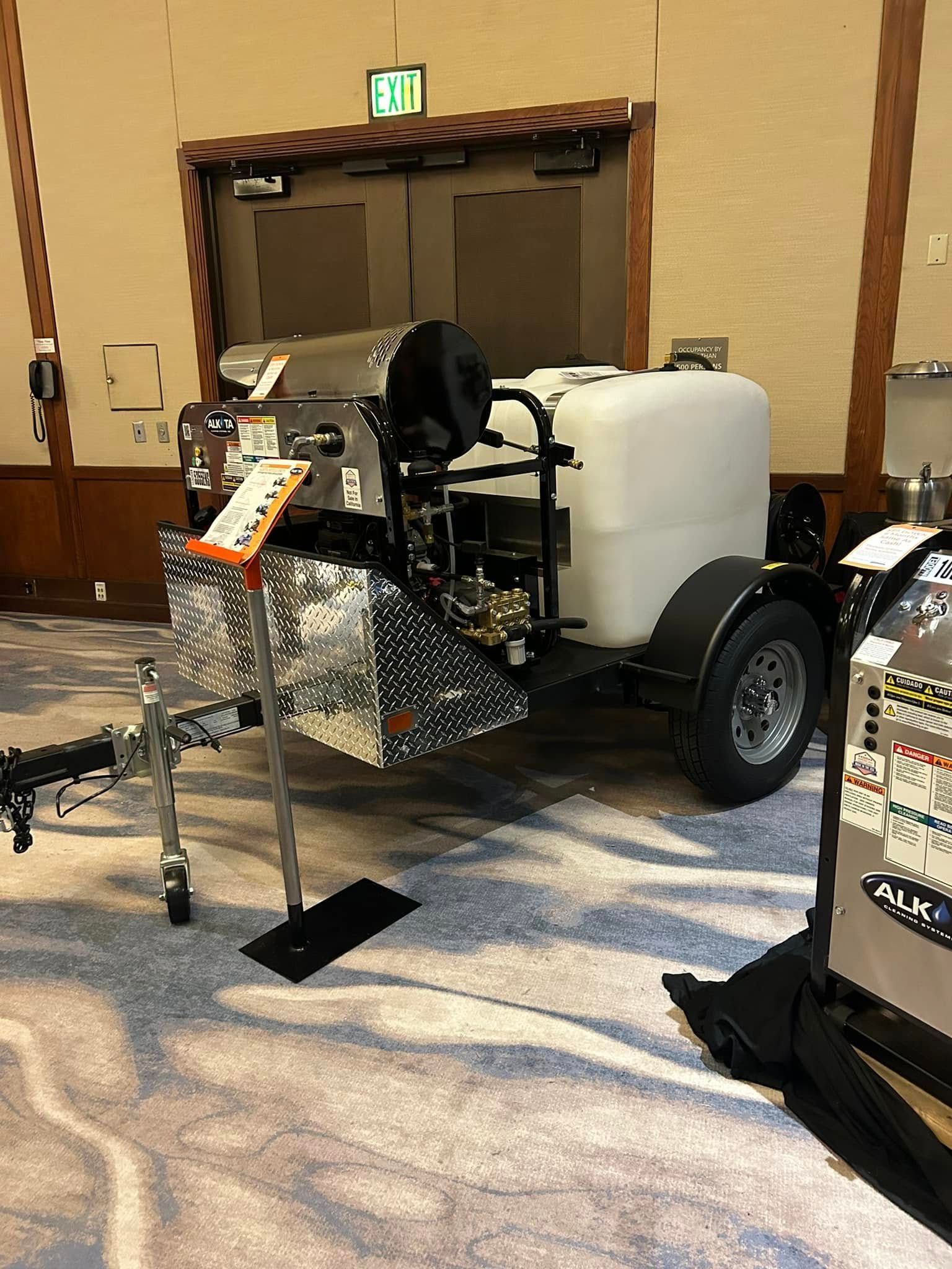 Compact utility vehicle with large white tank on display at an indoor event hall.