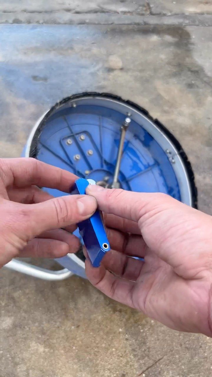 Hands holding a blue plastic tool over a blue wheel on a concrete surface