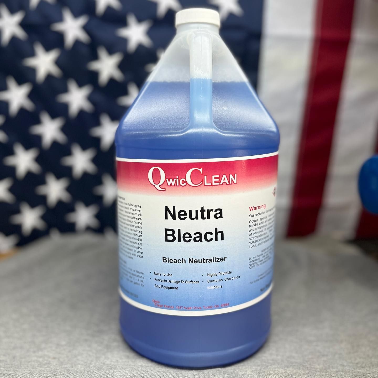 QwicLEAN Neutra Bleach bottle with blue liquid, standing in front of a U.S. flag backdrop
