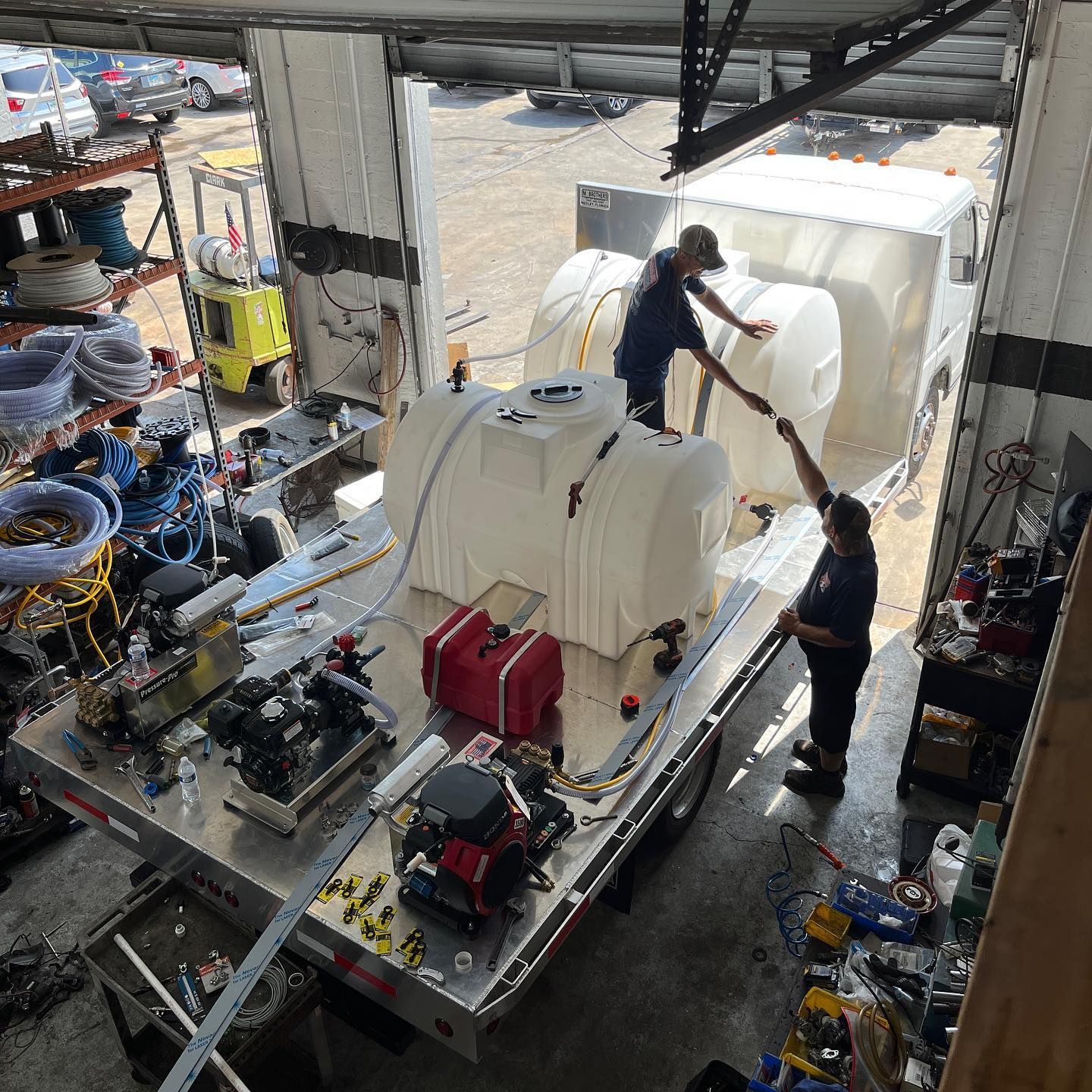 Workers assembling large white industrial equipment in a workshop, with machinery and tools surrounding them.