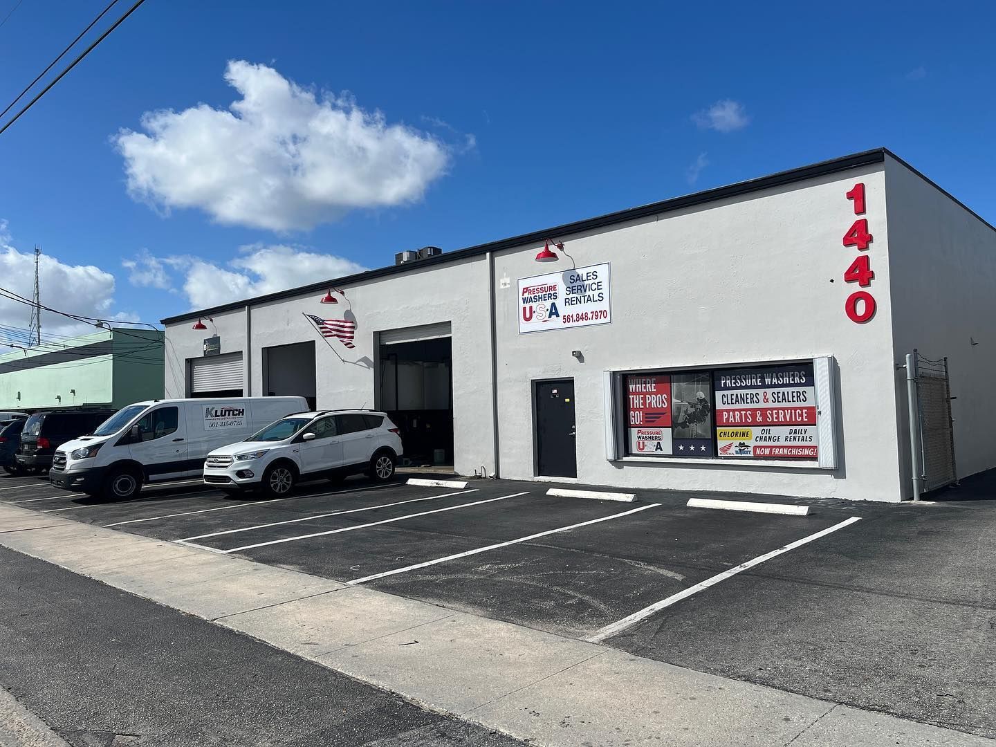 Small industrial building with parked cars, red number 140, and a bright blue sky.