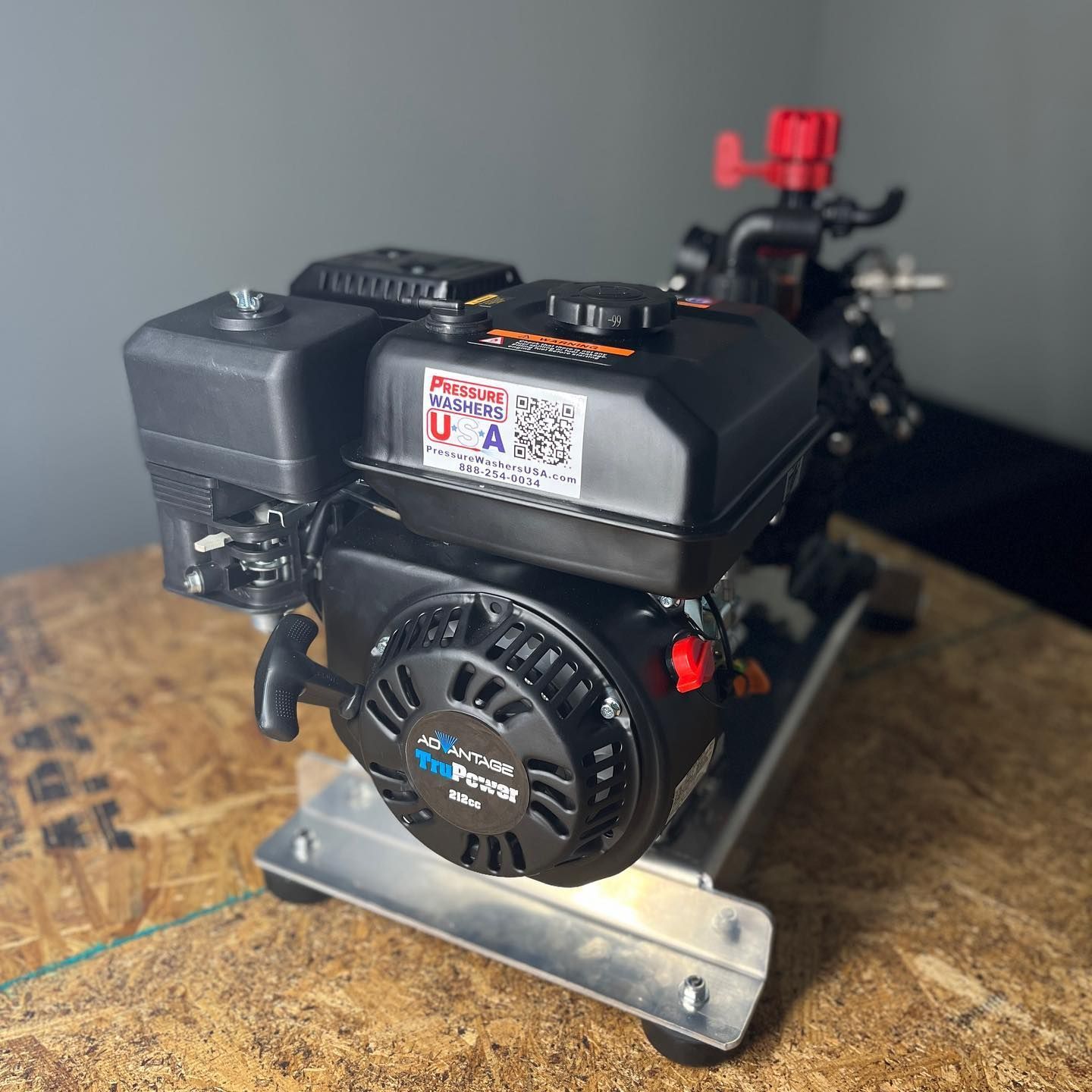 Small black gasoline engine on a metal base, shown on a wooden workbench with a red fuel cap.