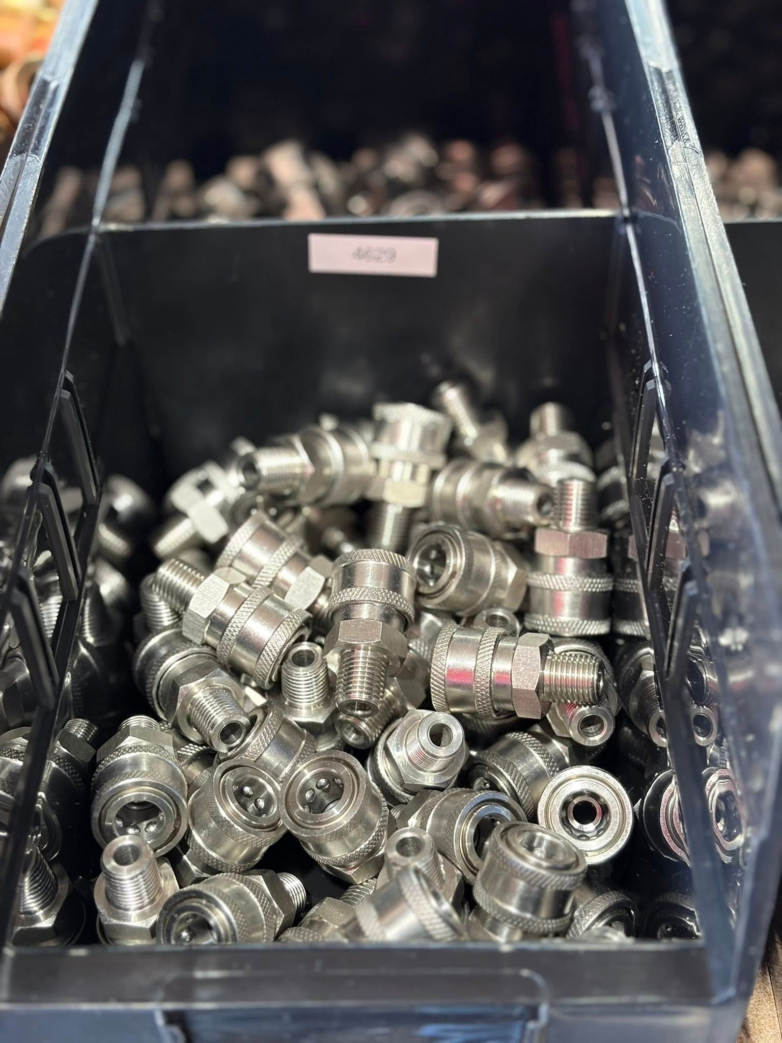 A bin filled with shiny metal fittings and connectors in a warehouse or workshop.