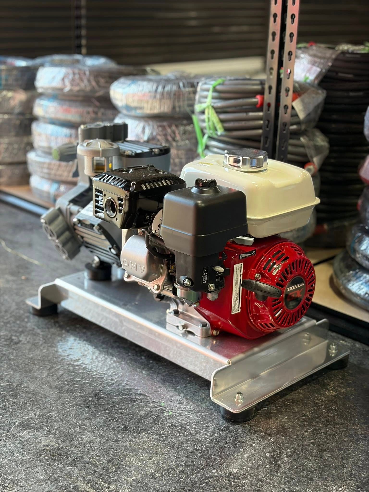 Small gas engine on a metal platform, with a red flywheel and white fuel tank in a workshop.
