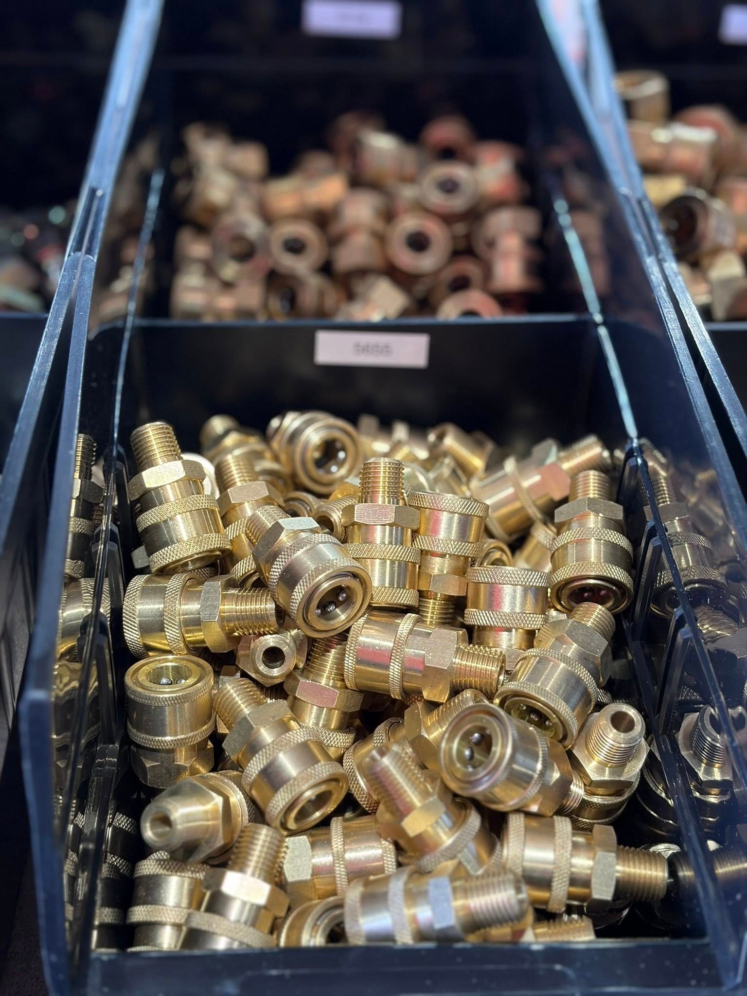 Bins of shiny brass pipe fittings and connectors in a warehouse or hardware supply area.