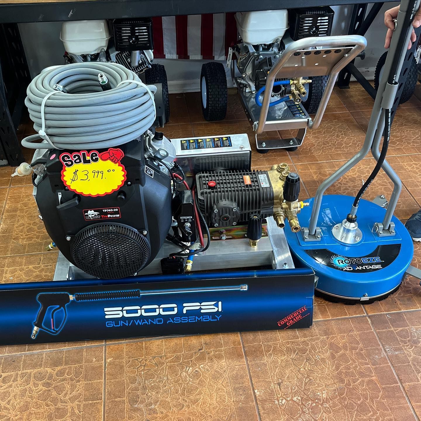 Pressure washer set with coiled hose, engine, and blue surface cleaner on a tiled floor.