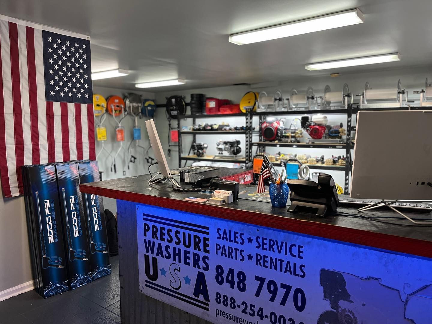 Pressure washer sales and service shop with blue-lit counter, tools, and American flag on the wall