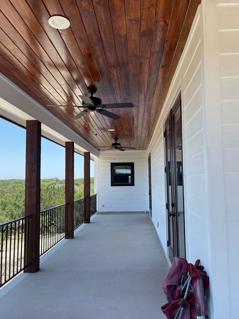 A large porch with a wooden ceiling and a ceiling fan.