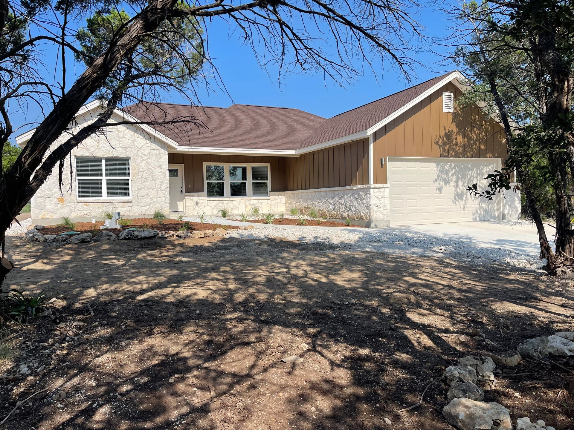 A white house with a brown roof is surrounded by trees.