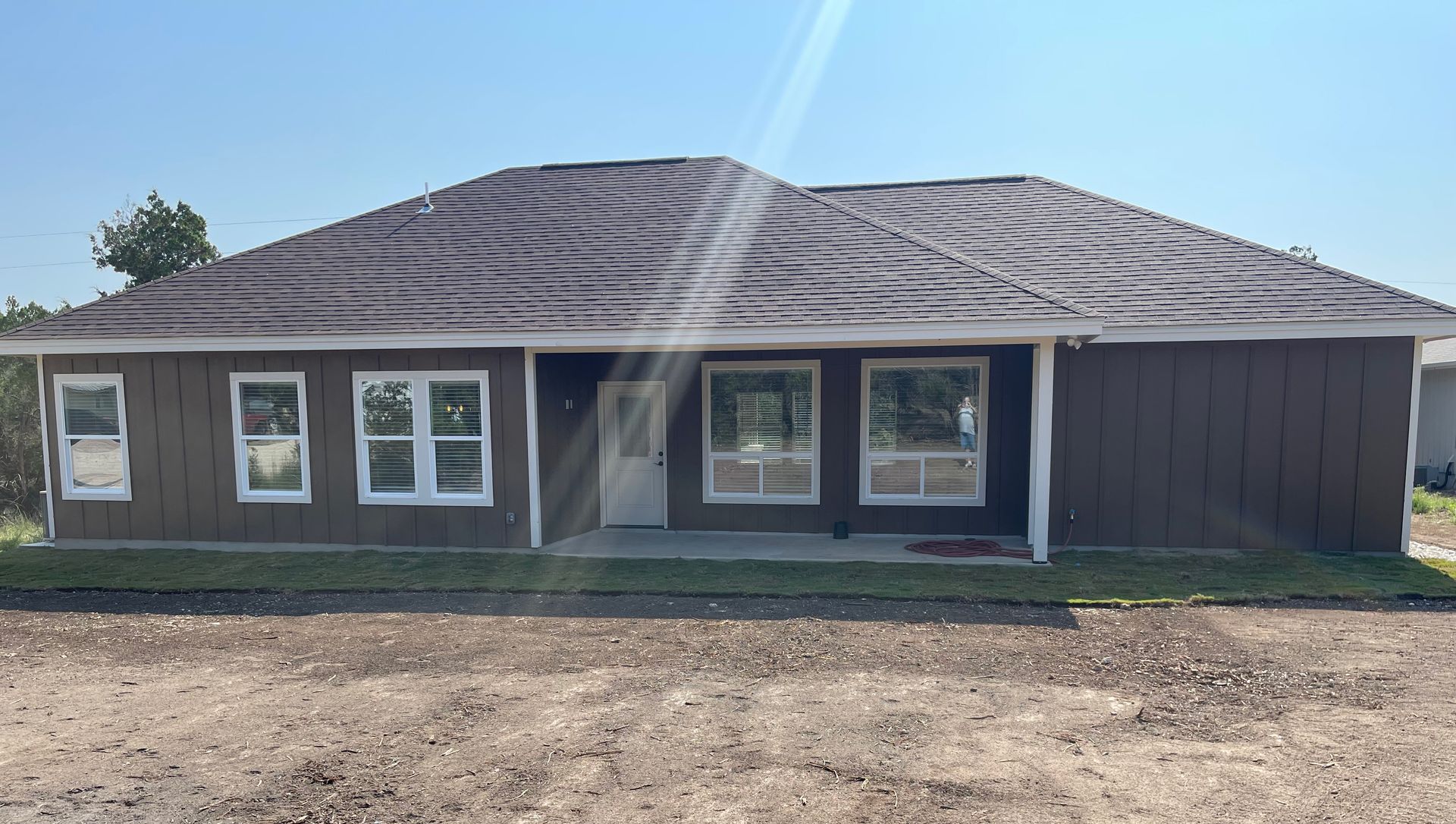 A brown house with a roof and a lot of windows is sitting on top of a dirt field.