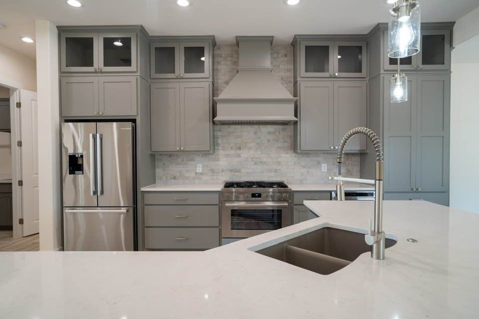 A kitchen with gray cabinets , stainless steel appliances , a sink and a refrigerator.