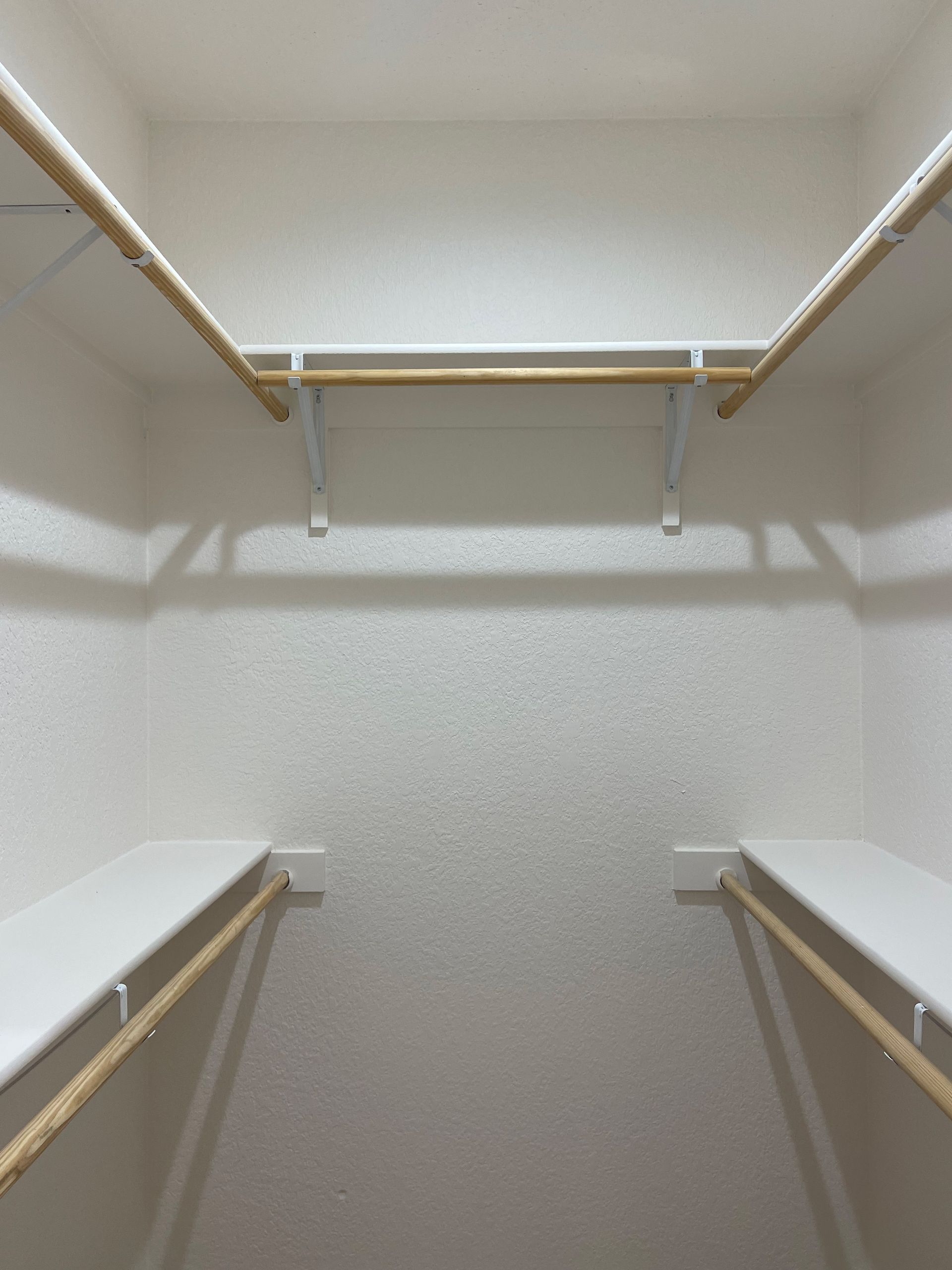 An empty walk in closet with shelves and wooden rods.