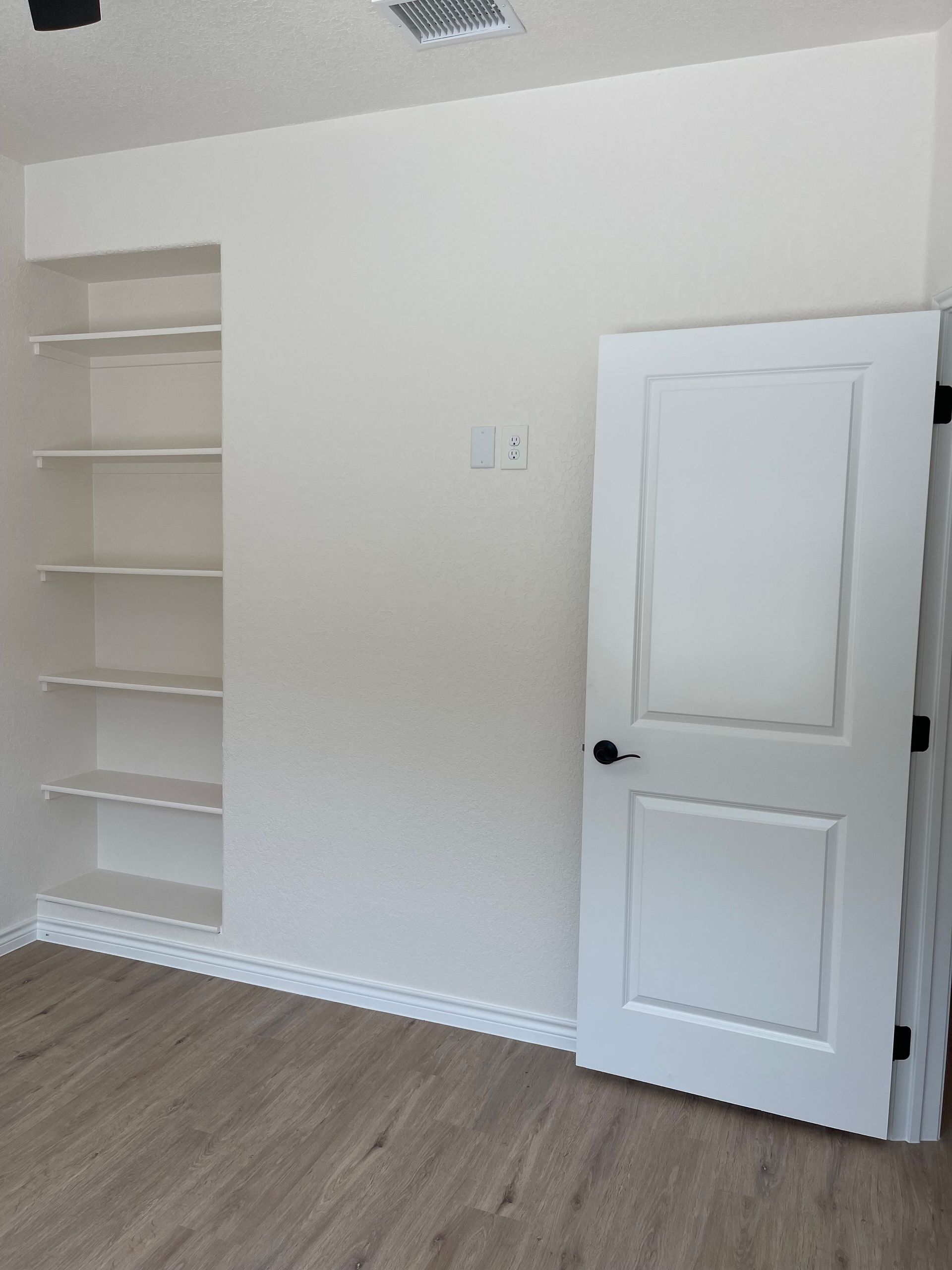 An empty room with a white door and shelves