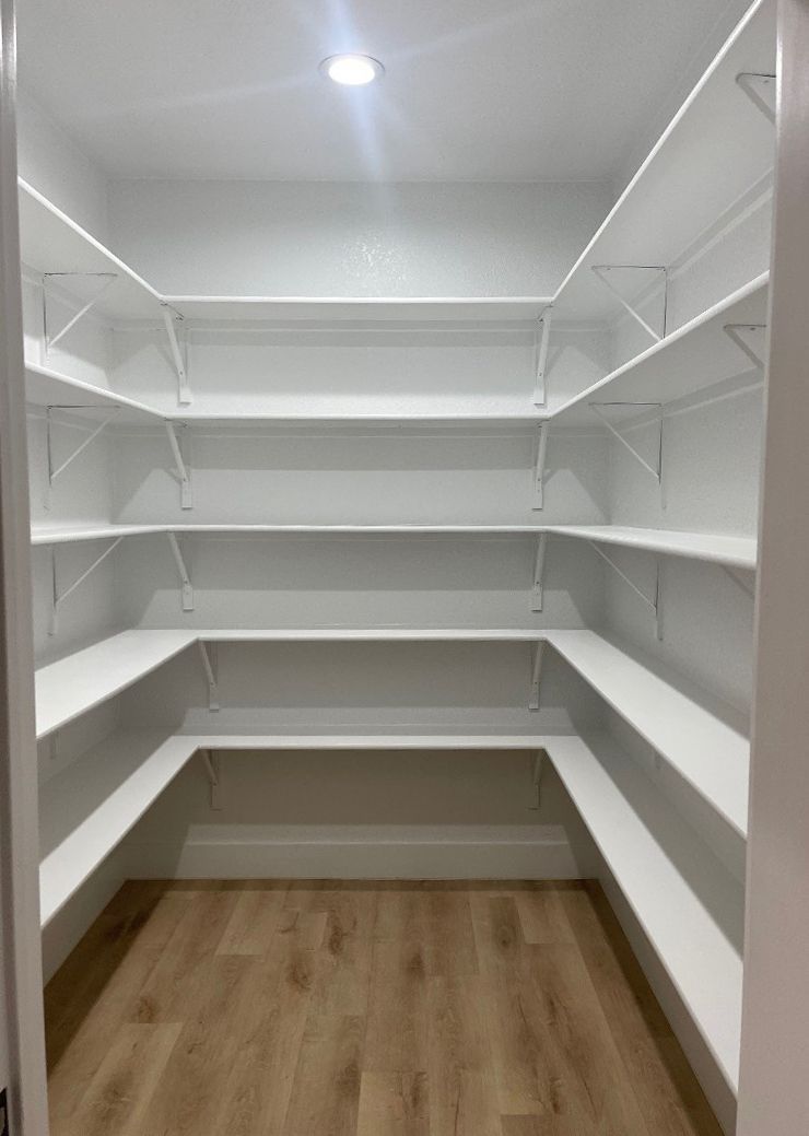 A walk in pantry with wooden floors and white shelves.