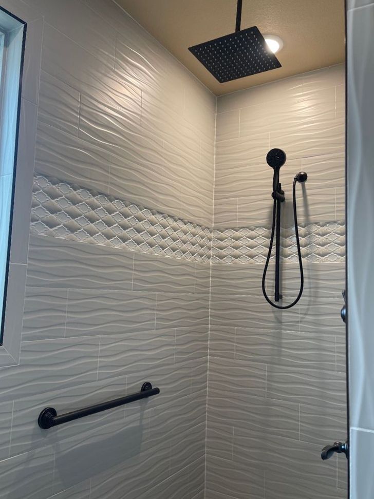 A shower with white tiles and a black shower head.