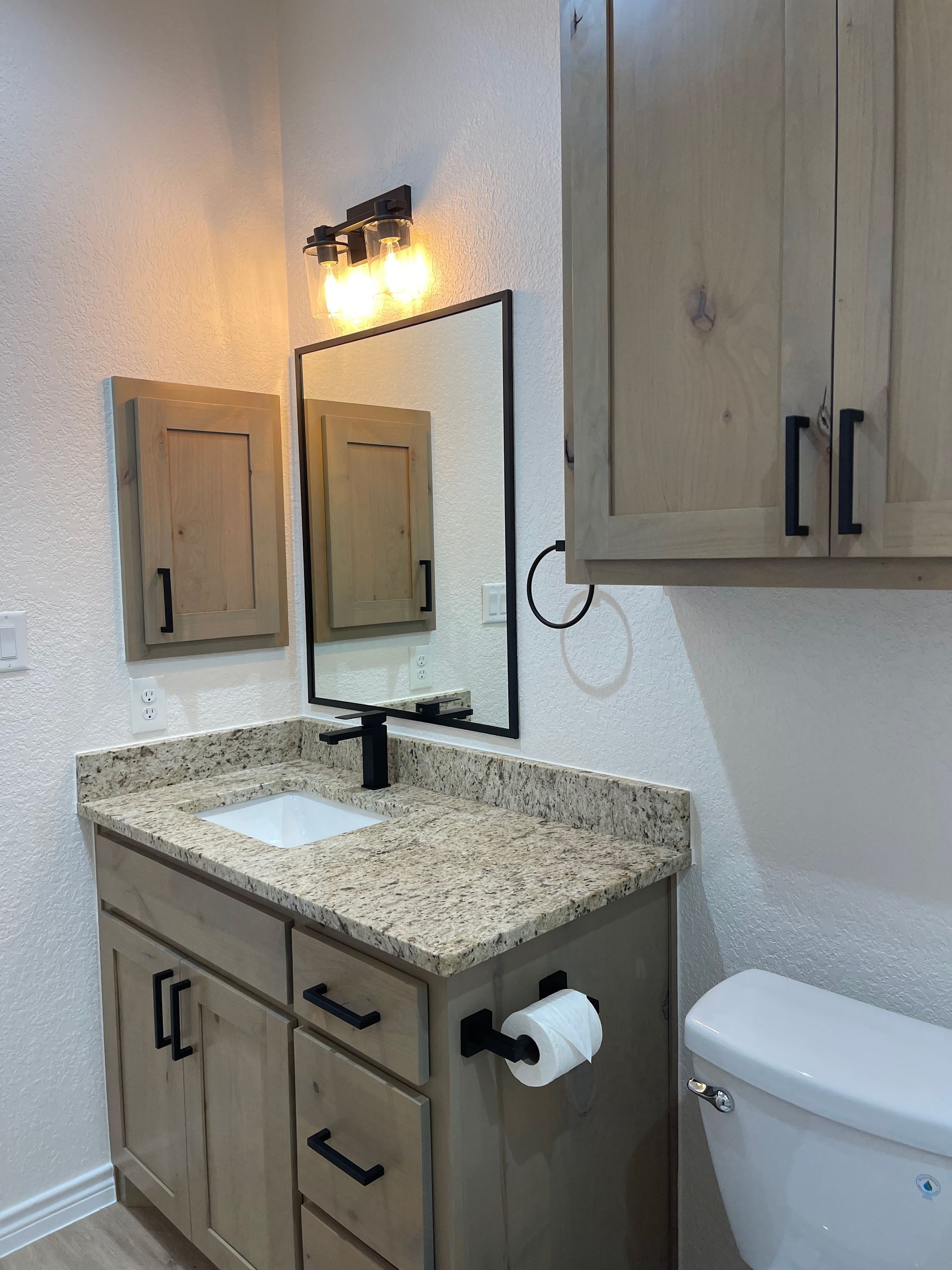 A bathroom with a sink , toilet , mirror and cabinets.