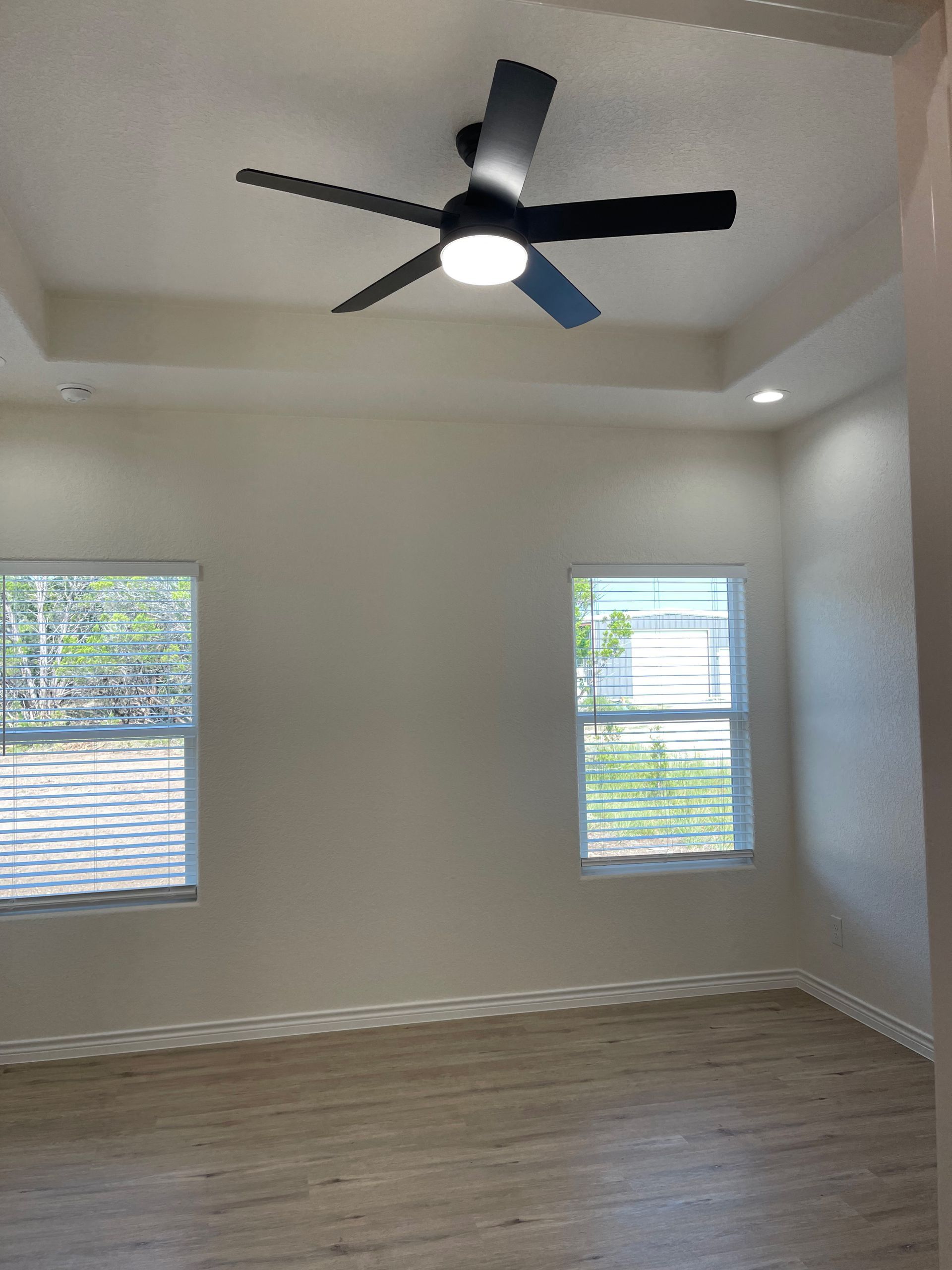 An empty room with a ceiling fan and two windows