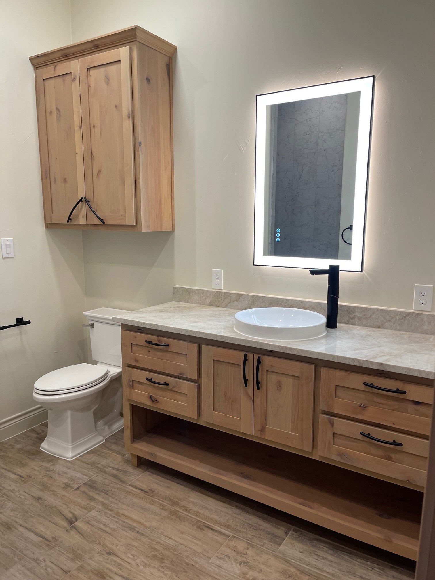 A bathroom with a toilet , sink , mirror and wooden cabinets.