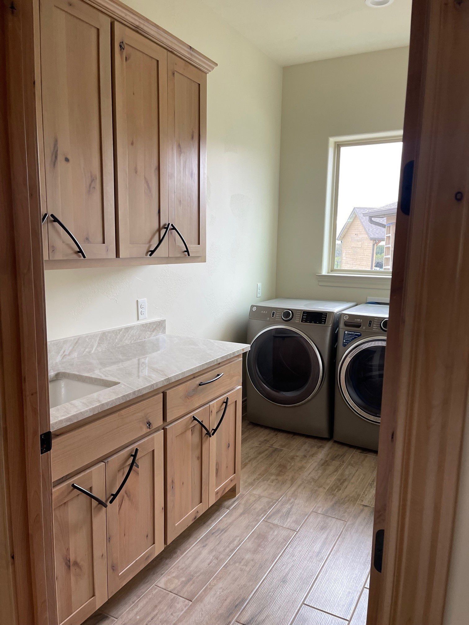 A laundry room with a sink , washer and dryer , and wooden cabinets.