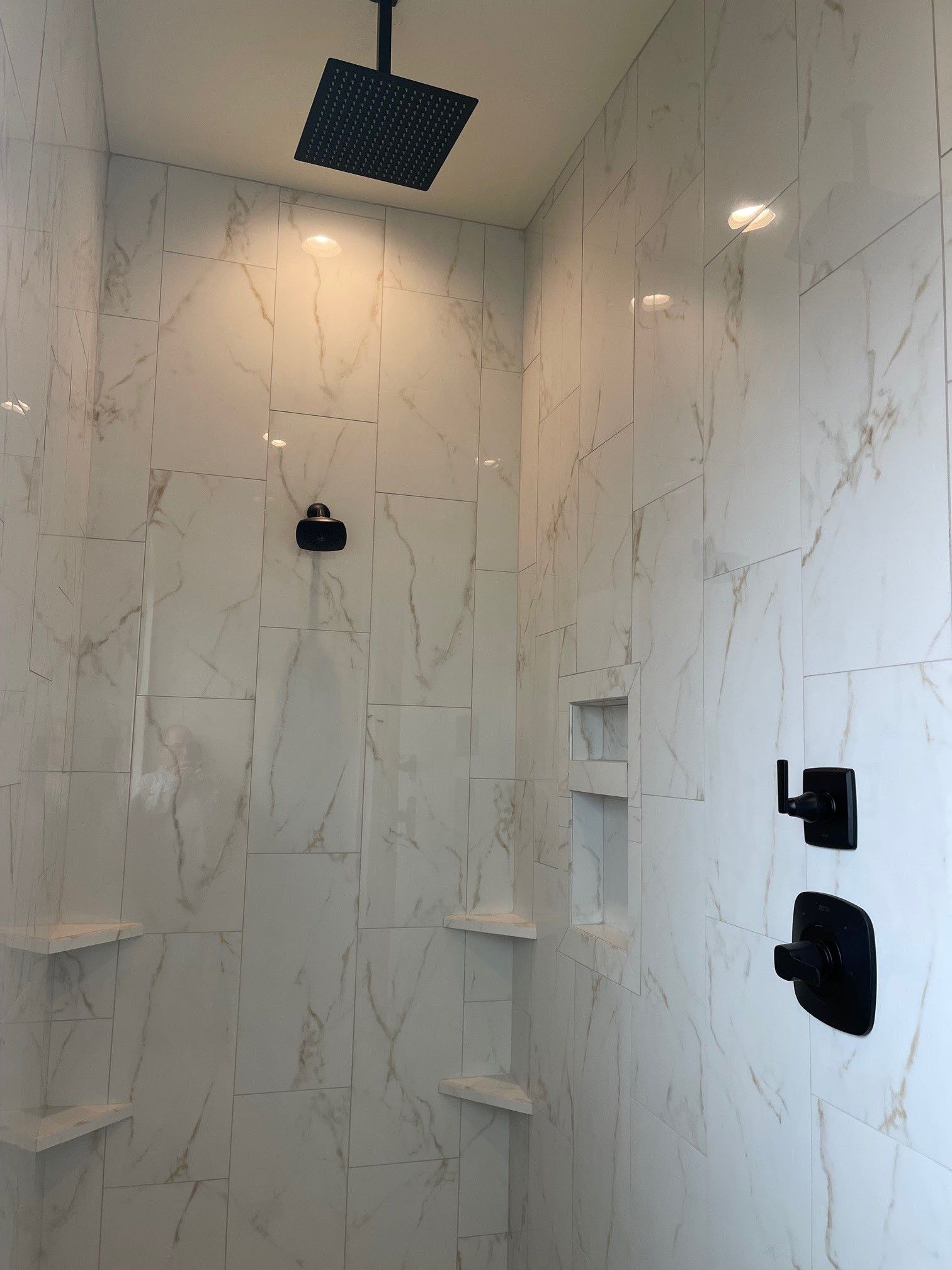 A shower with white tiles and a black shower head.