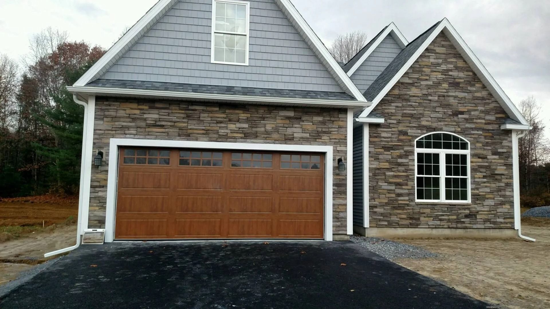 New suburban house with gray siding, stone facade, and brown two-car garage on a paved driveway.