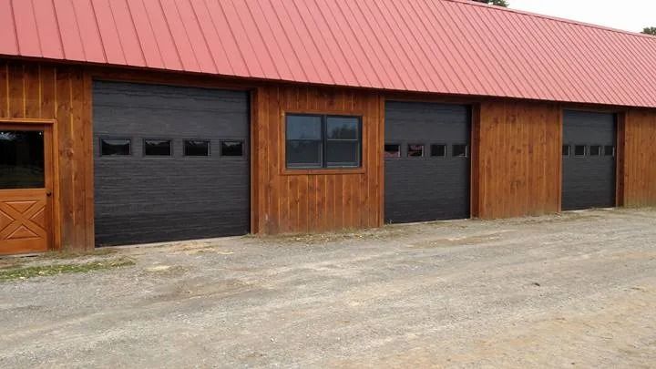 Exterior of a wooden building with black garage doors and a red metal roof