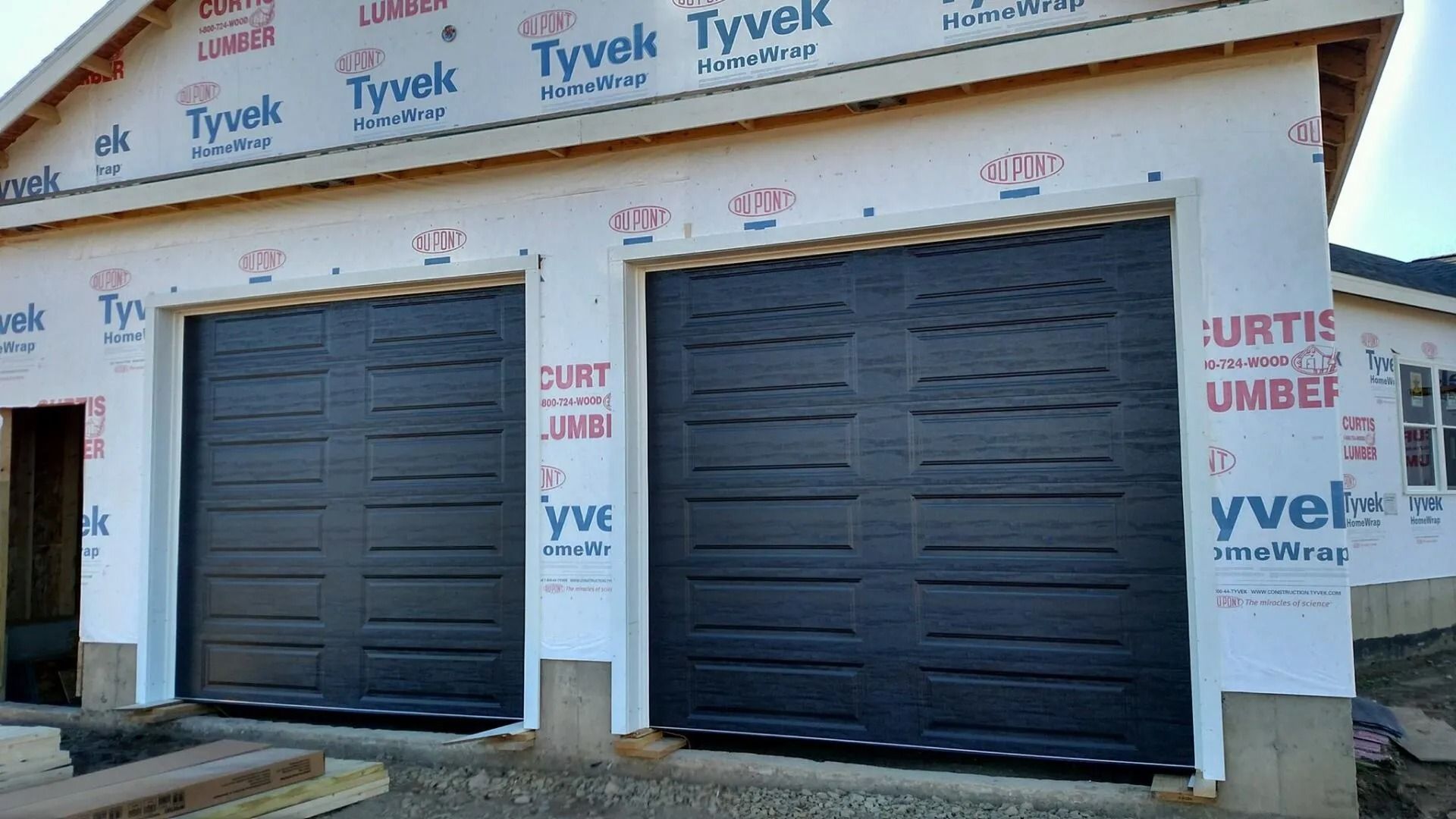 Two dark gray garage doors in a building under construction with Tyvek wrapping on the walls.