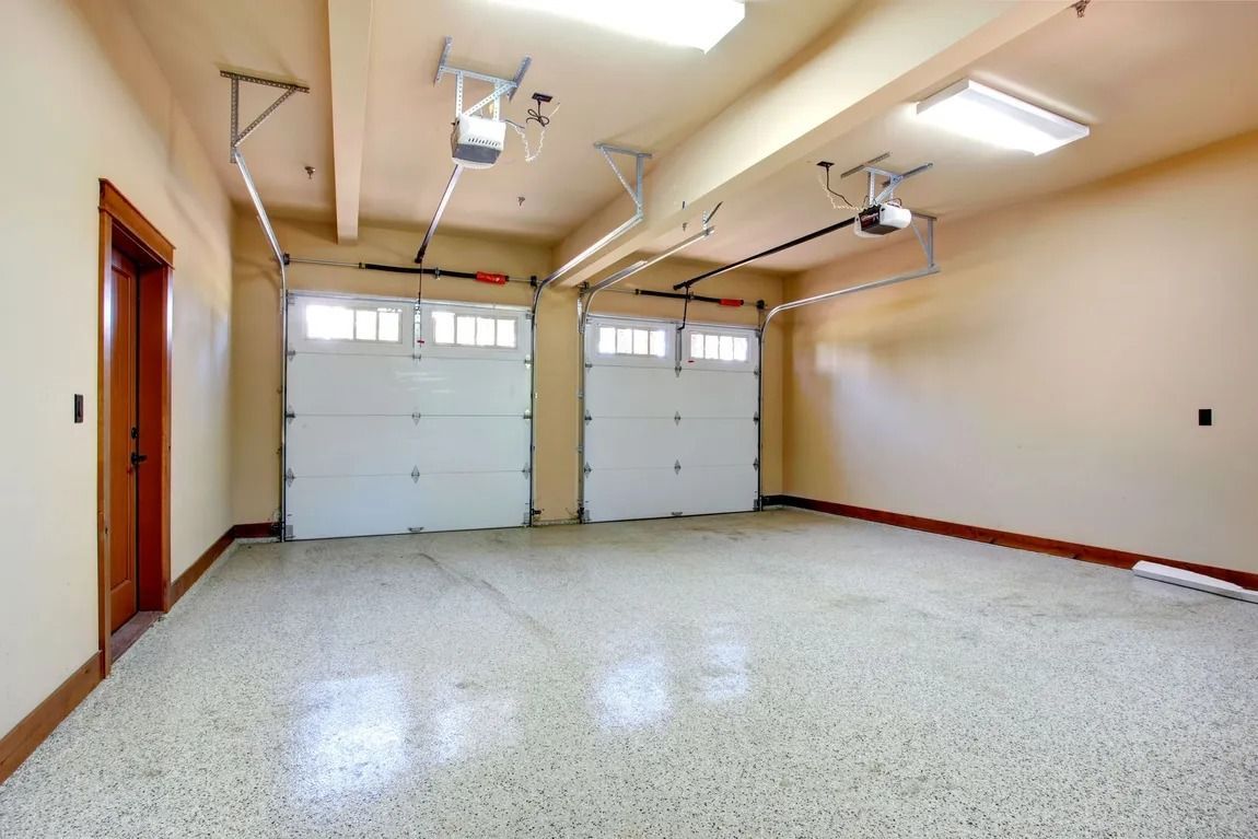 Empty two-car garage with white doors, speckled floor, and beige walls.