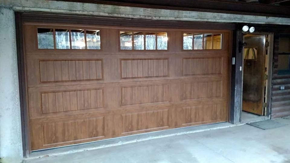 Wooden garage door with three small windows, set in a covered driveway beside a side entrance.