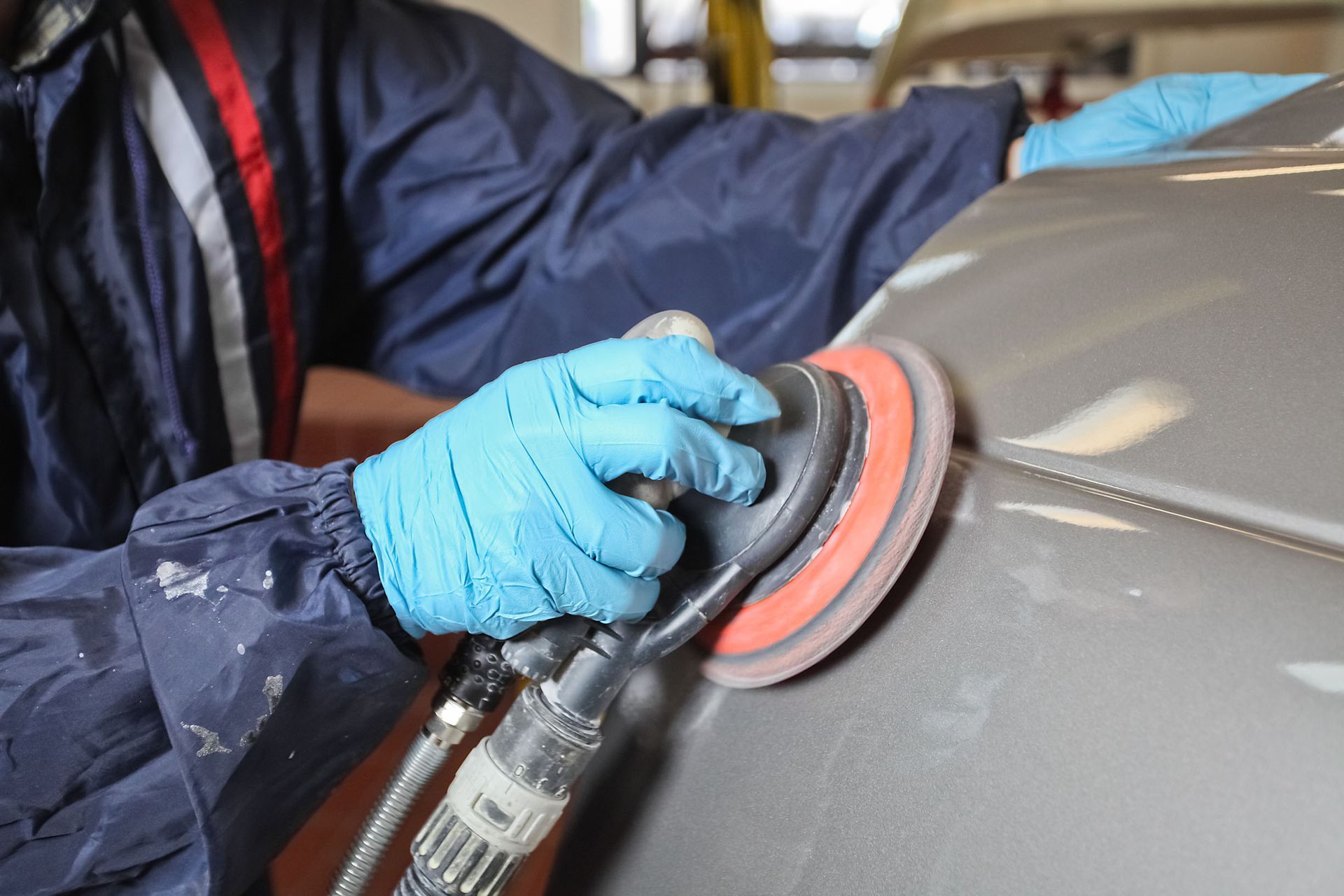 Gloved hands sanding a gray car panel with a power polisher