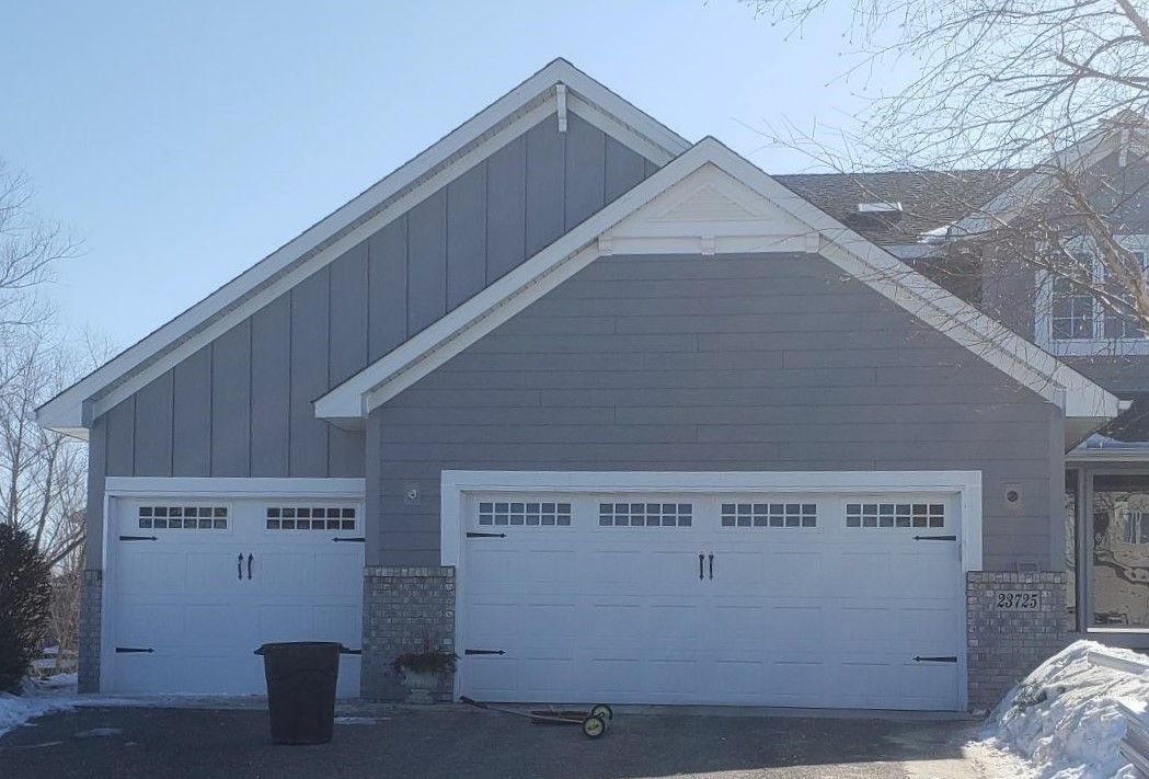 A house with two garage doors and a trash can in front of it.