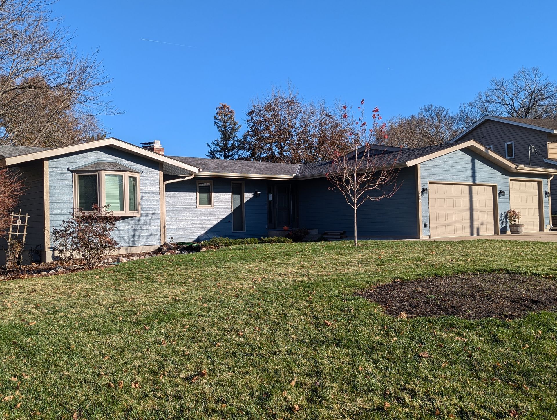 A house with two garages is sitting on top of a lush green field.