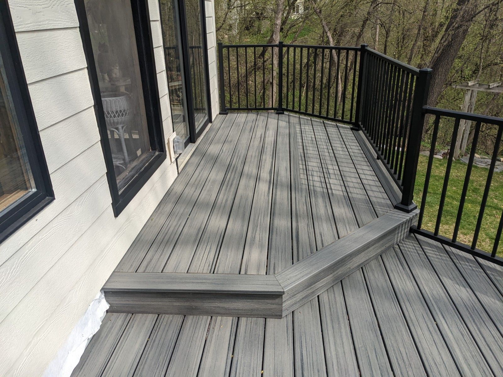 A gray deck with a black railing and stairs on the side of a house.