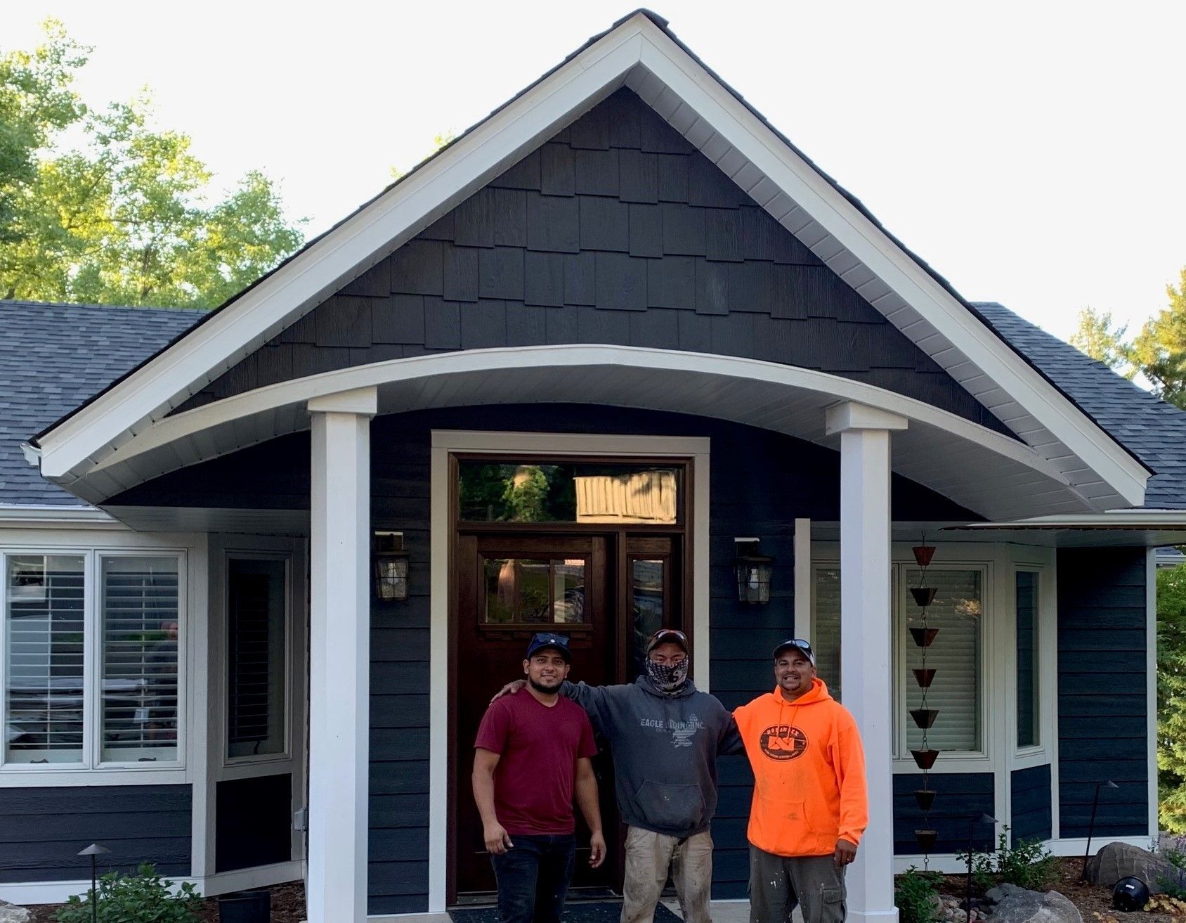 Three men are standing in front of a blue house.