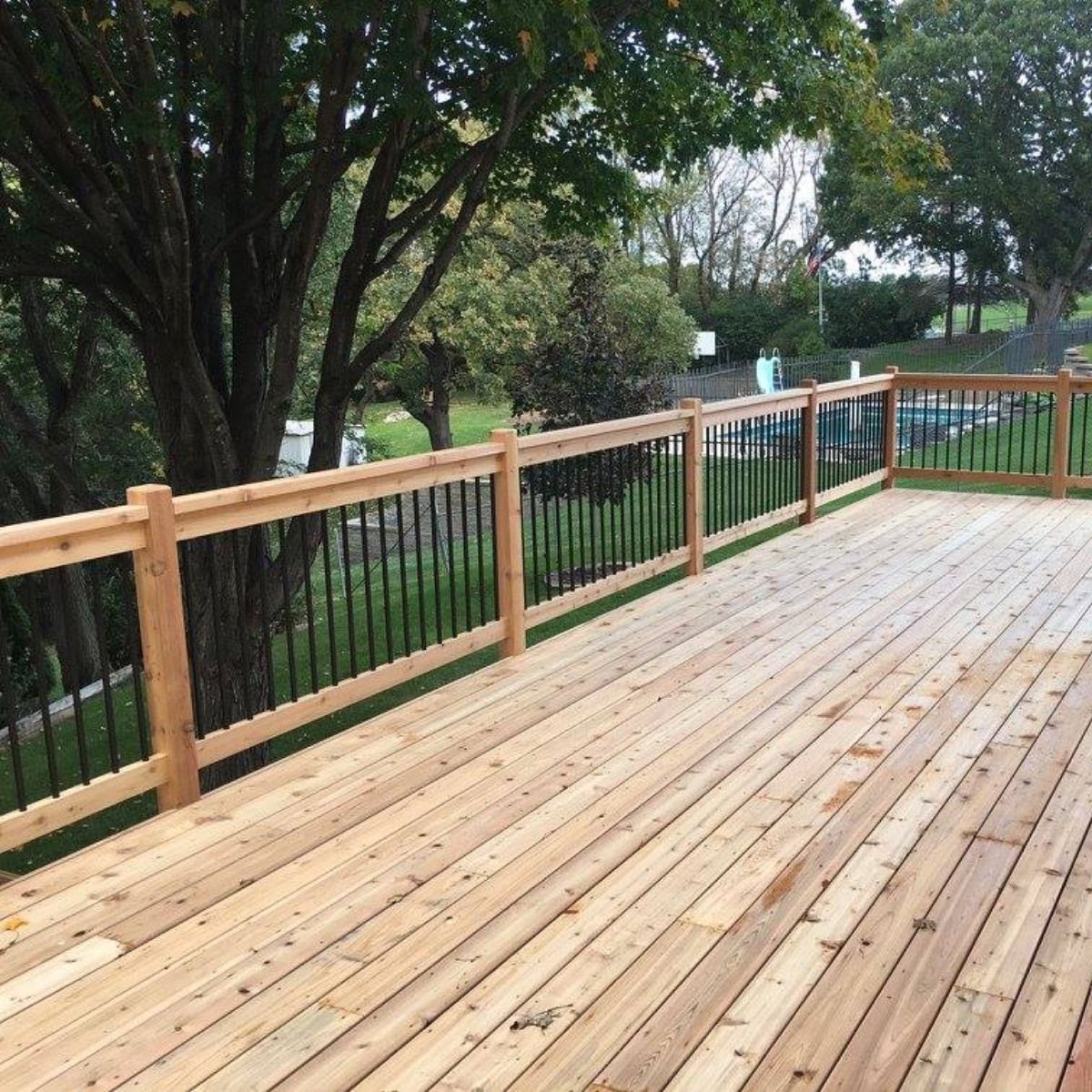 A wooden deck with a metal railing and trees in the background