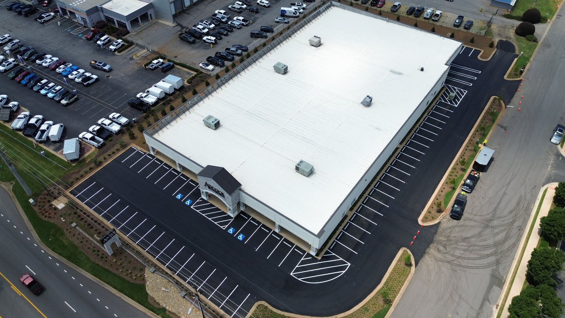 Aerial view of a car dealership building with a white roof and adjacent parking lots filled with cars.
