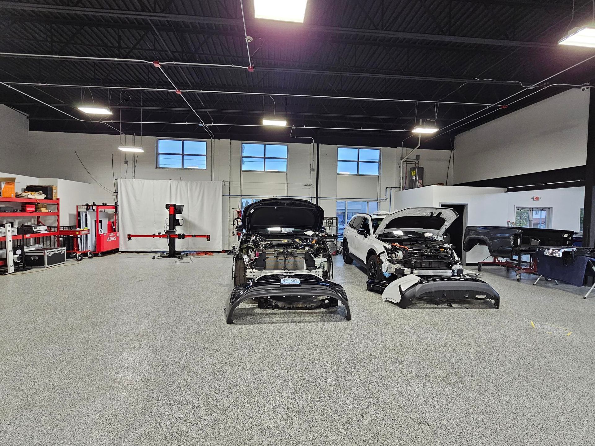 Two cars are parked in a garage with their hoods open.