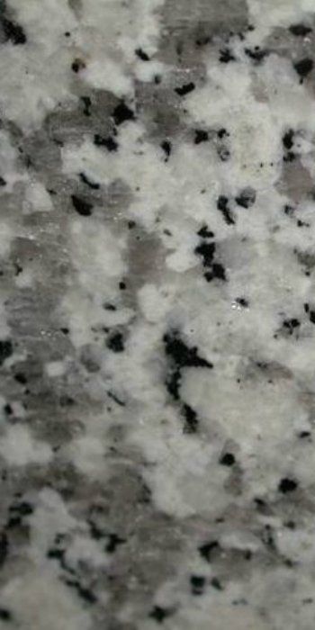 A close up of a white granite counter top with black spots.