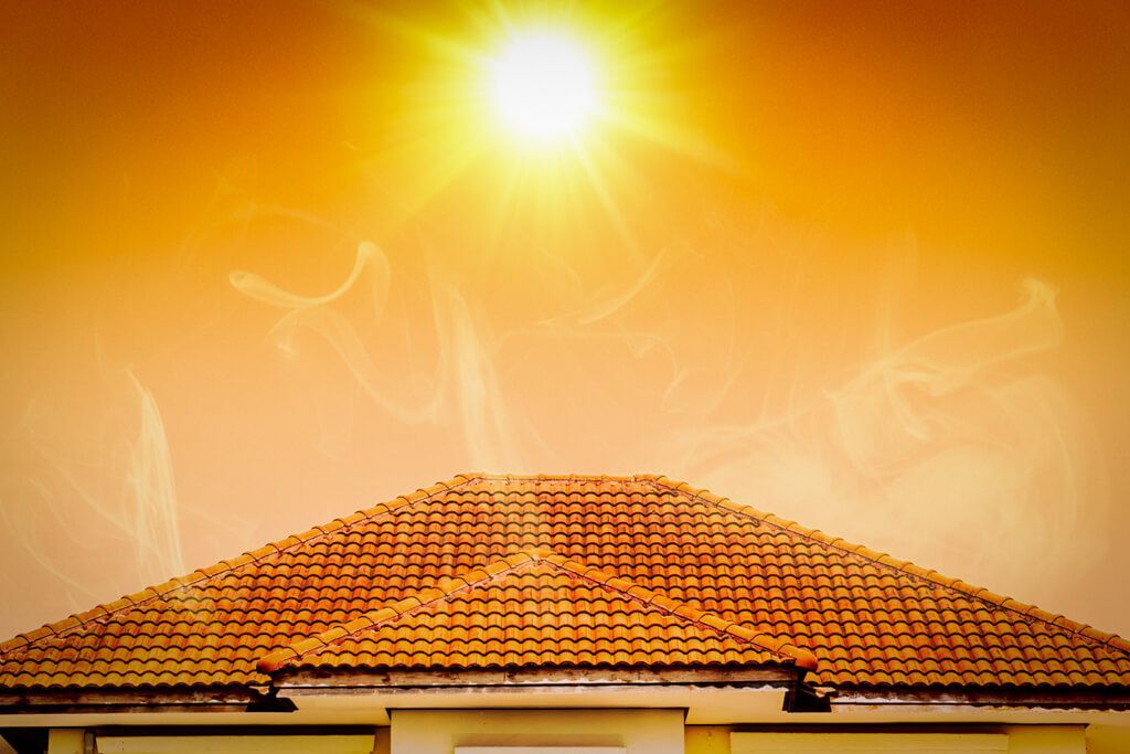 A bright sun shines in a golden, hazy sky above the terracotta tiled roof of a house.