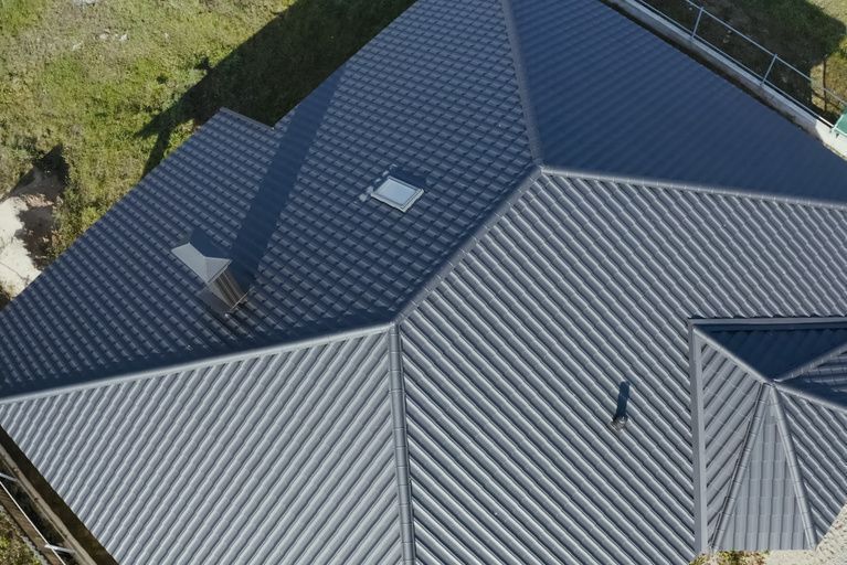 Aerial view of a residential roof with a mix of dark gray metal corrugated and shingled roofing sections.