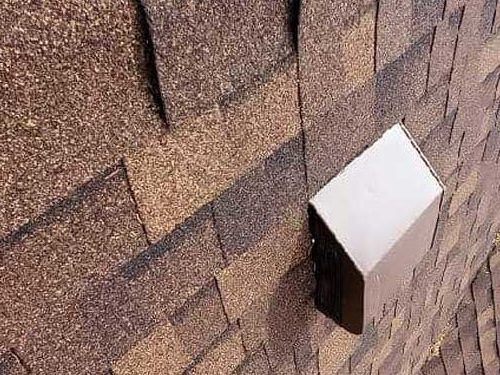 A rectangular metal roof vent sits mounted on a sloped surface covered with brown, multi-toned asphalt shingles.