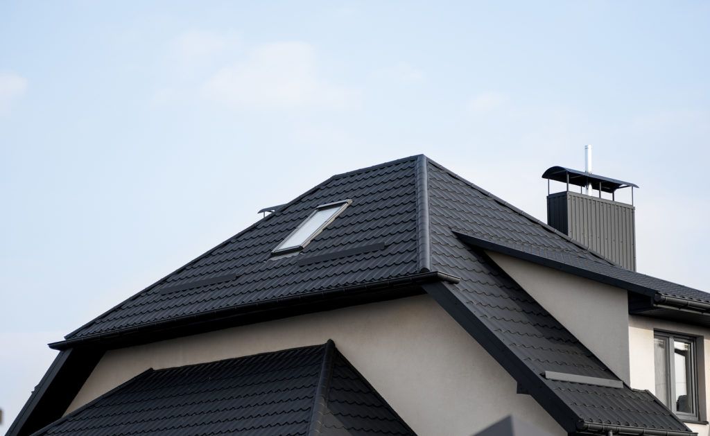 A black-tiled roof with a skylight and chimney against a clear blue sky.