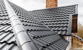 A close-up view of a dark gray, corrugated metal roof with a chimney in the background.