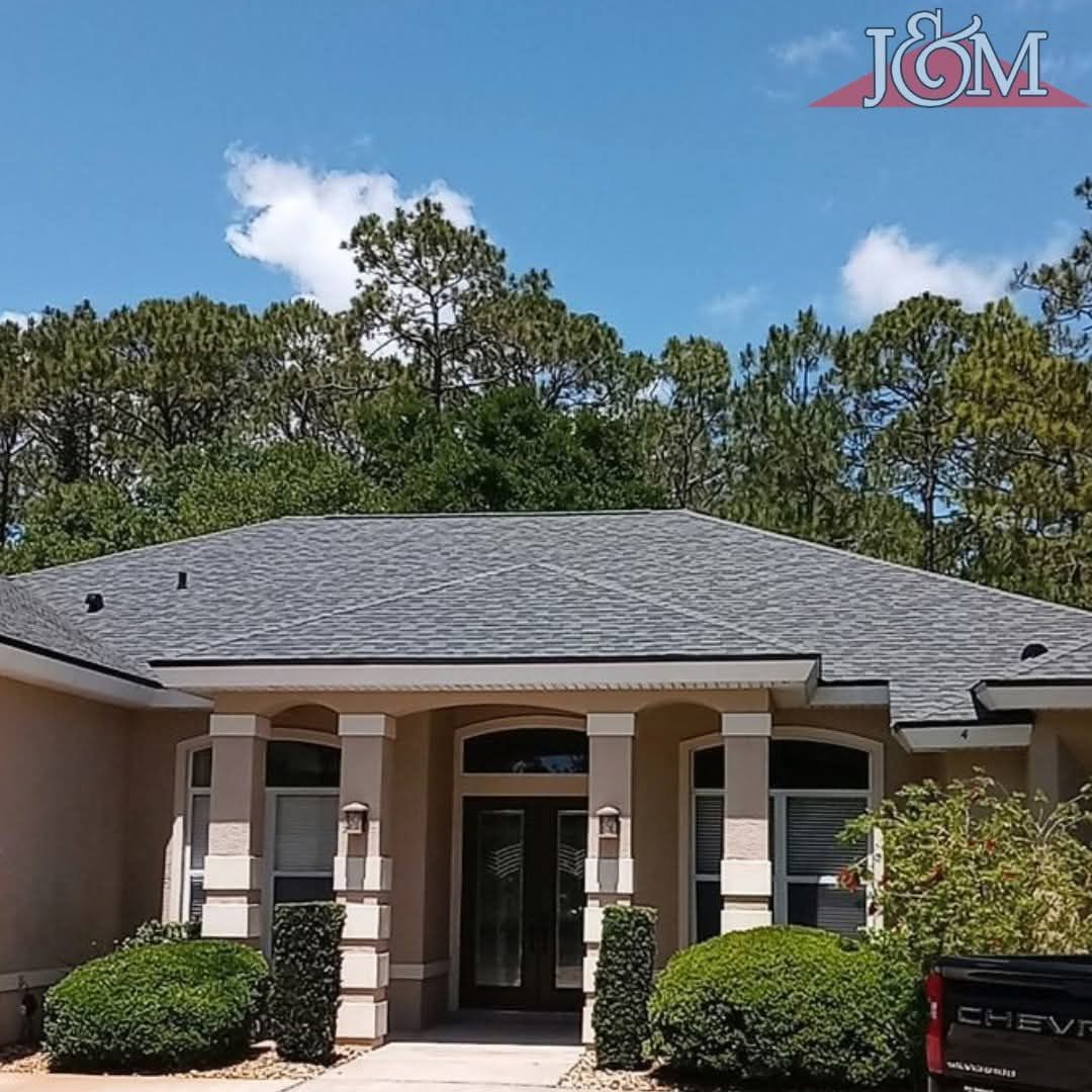 Tan single-story house with a grey roof, arched windows, and a front porch supported by square pillars.